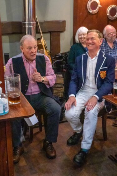 Michael Portillo laughing at a pub table, as Fraser Bruce sings