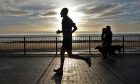 Members of Arbroath Footers Run Club run along the seafront in Arbroath, silhouetted against the sun.