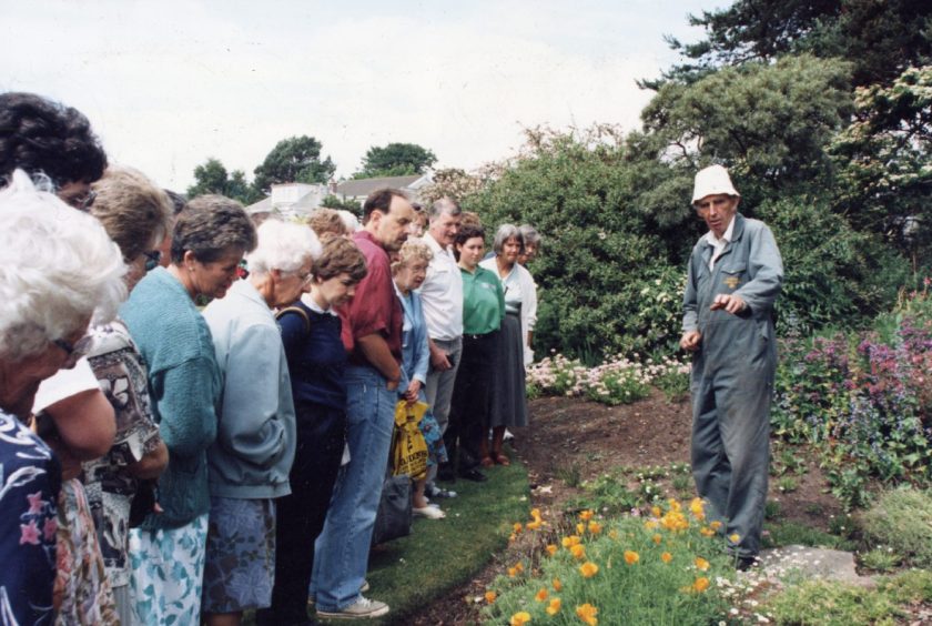 People listen to a man standing ina flowerbed giving a talk on Barnhill Rock Garden Open Day in July 1995.