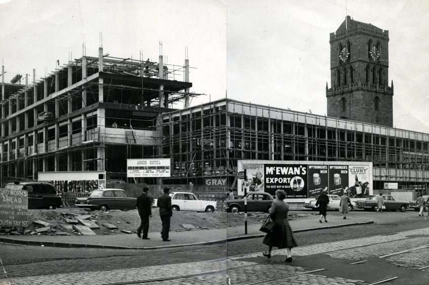 People cross the road while, in the background, the Angus is being constructed in 1963. 