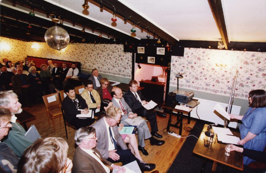 A crowd sitting listening to a speaker at the front of the hotel. 