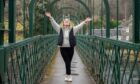 Daisy Walker arms raised on green suspension bridge in Pitlochry