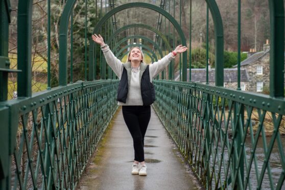 Daisy Walker arms raised on green suspension bridge in Pitlochry