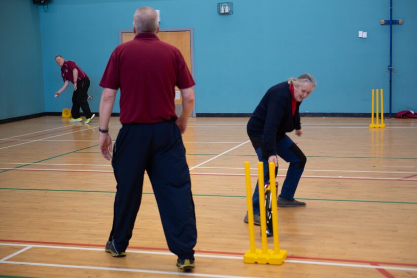 Three older people playing cricket in gymnasium
