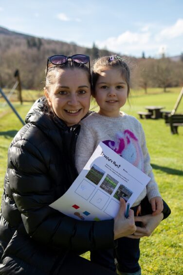 Mother and child Erika and Maeve Fabian holding treasure hunt clue sheet in green park at Kenmore