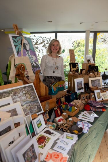 Kathy Burns beside a stall featuring various art and crafts in Birnam Arts
