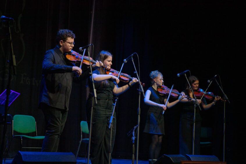Young fiddle players on stage in darkened auditorium