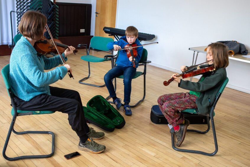 Amy Geddes working with two young children playing fiddles