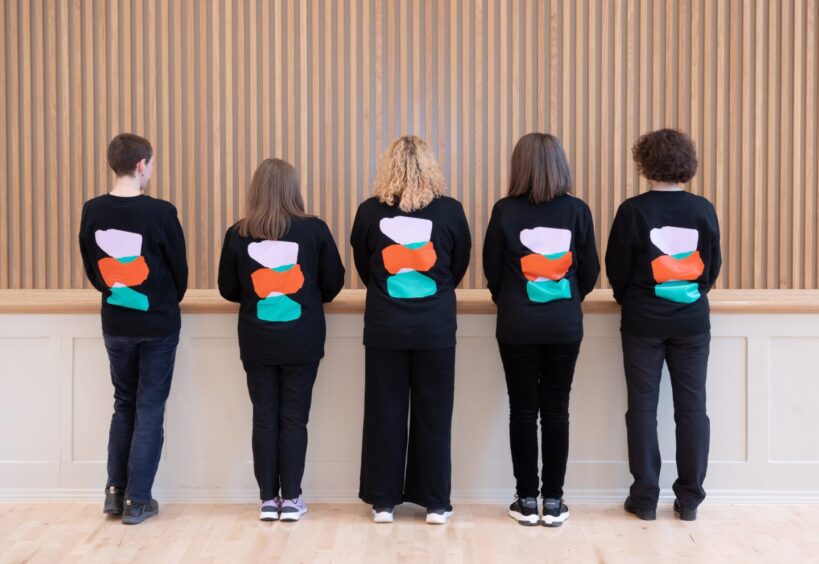 Perth Museum staff with backs turned, showing black uniforms with red, orange and blue coloured stonses.