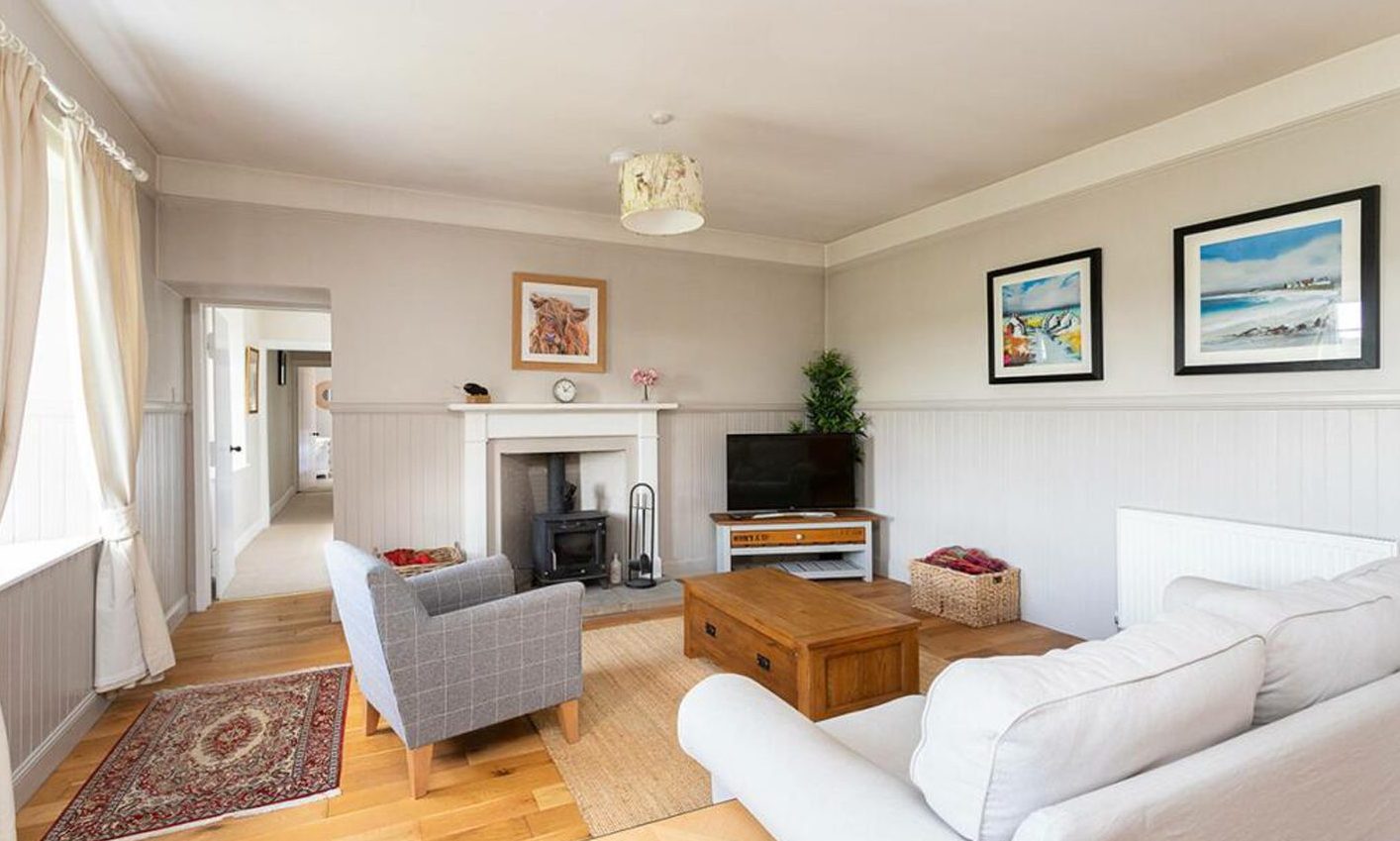 The living room at the Lundie cottage, with a white couch, grey armchair, fireplace and paintings on the walls