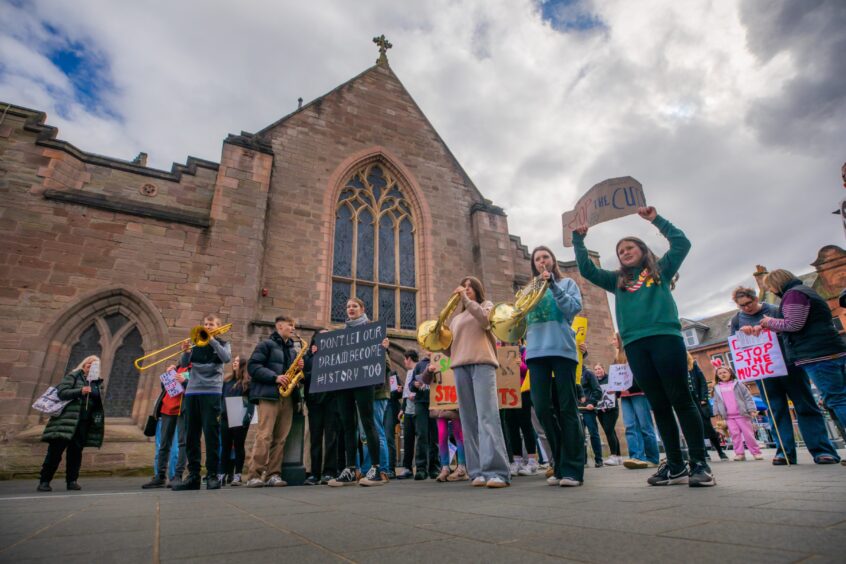 Youngsters playing instruments and holding placards outside Perth Museum