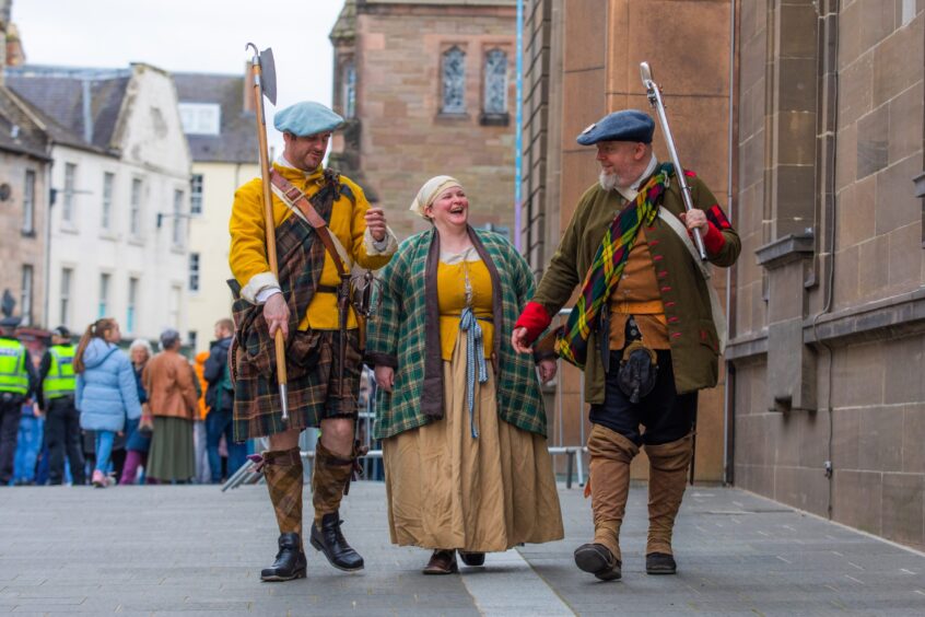 Three people from the Gael History group dressed as Jacobites walking past St Johns Kirk and the new Perth Museum with crowds behind them