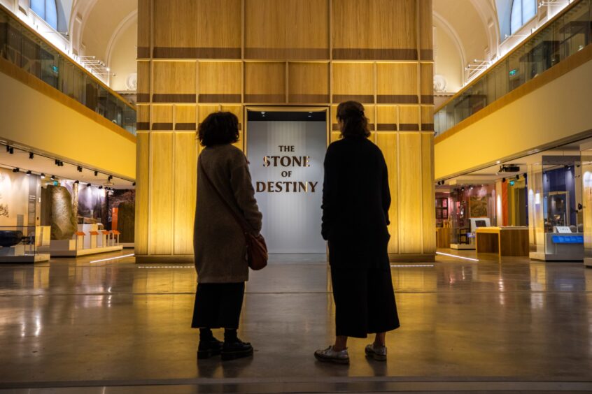 Two people, backs to camera, standing in front of The Stone of Destiny Experience at Perth Museum
