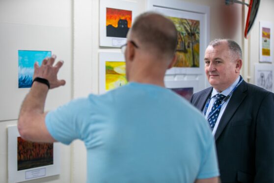 Perth prison governor Andy Hodge talking to one of the artists in front of a wall of paintings