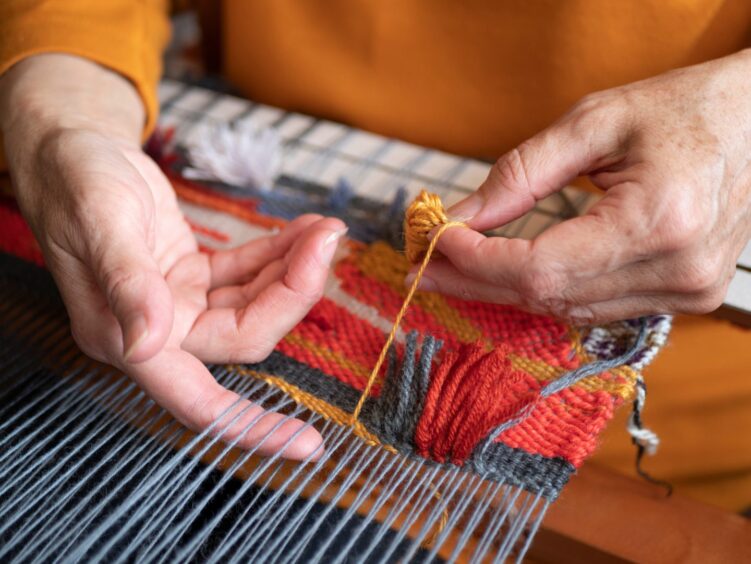 Master weaver weaving a tapestry with diverse bright threads, close up