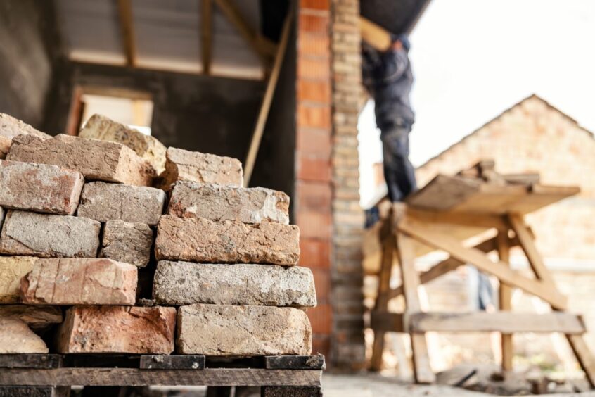 Focus on a bricks with housebuilder building a house in a blurry background