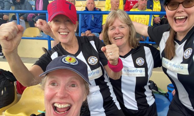 Four women in black and white Jeanfield Swifts football kits celebrating in football stadium