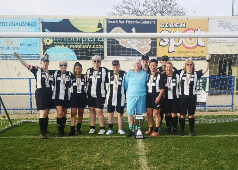 Jeanfield Swifts women's walking football team in black and white striped football kit posing for team photo in goal mouth.