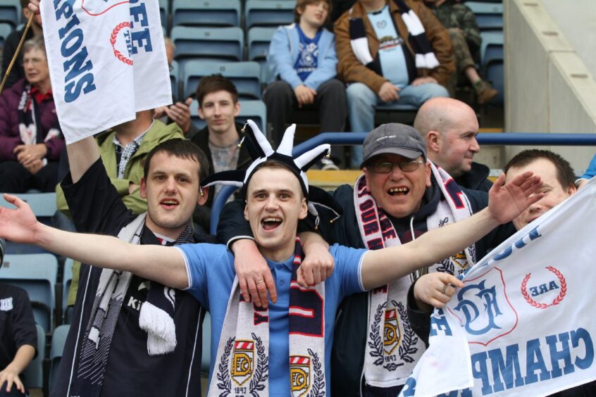 Dundee fans with flags celebrate in the stand after the final whistle