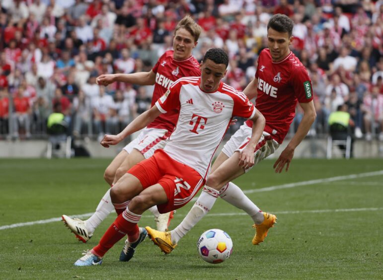 Jamal Musiala keeps the ball for Bayern Munich against two FC Cologne opponents.