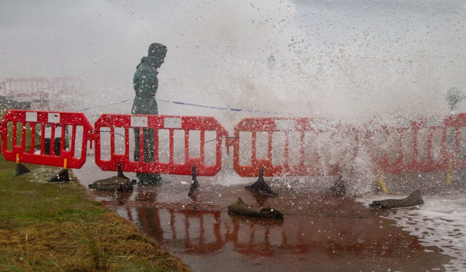 A person walks past a barrier on Montrose seafront as a storm sends up spray.