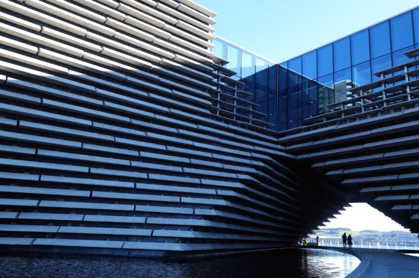 Image shows the outside of the V&A Dundee, where you can see it's unique design as well as some of the glass portion of the structure and the water around the bottom of the building.