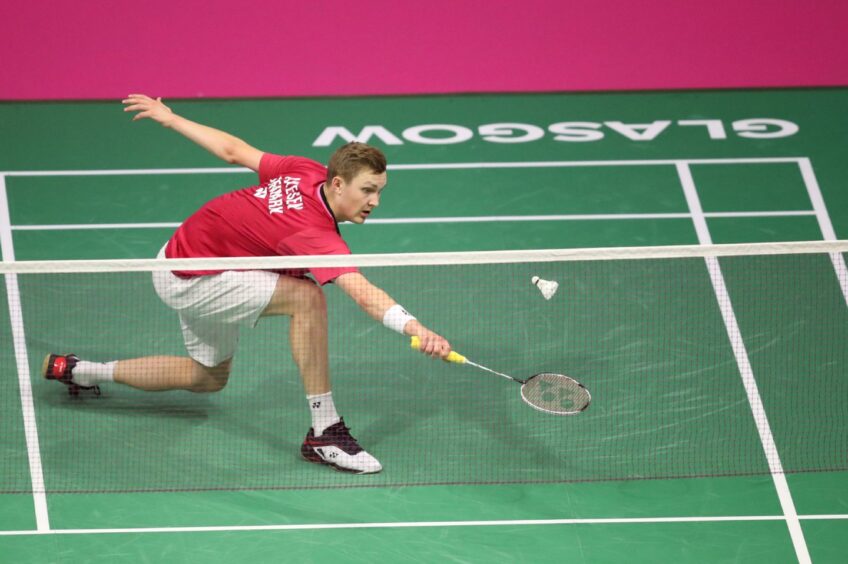 Denmark's Viktor Axelsen reaching for shot on badminton court with Glasgow written on edge