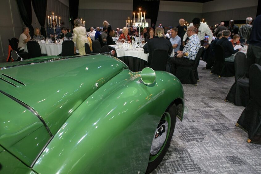 People seated for dinner with bonnet of green classic car in foreground