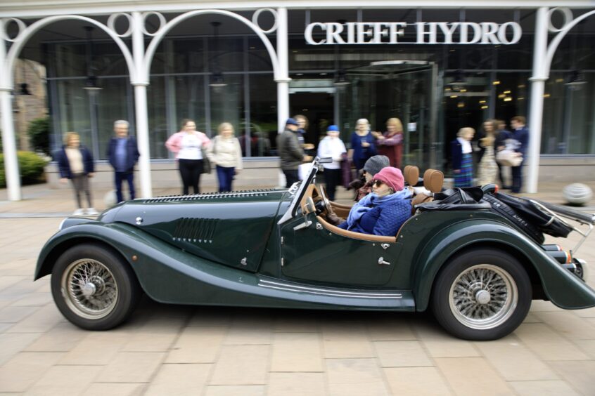 Green open topped Morgan car with two people inside driving past crowd outside Crieff Hydro Hotel reception