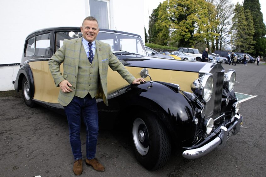 Smiling man in tweed jacket standing next to 1955 Rolls Royce Silver Wraith