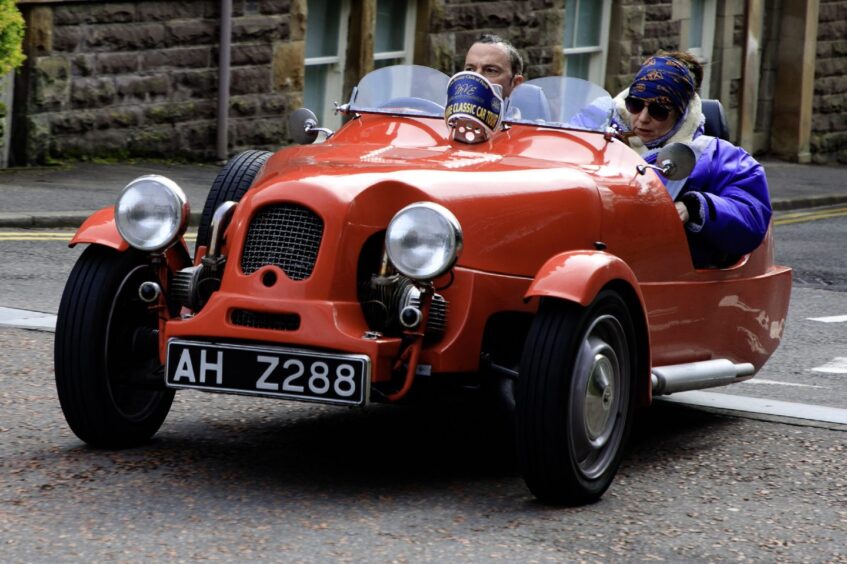 Two people in a three-wheeled red kit car, with two wheels at front