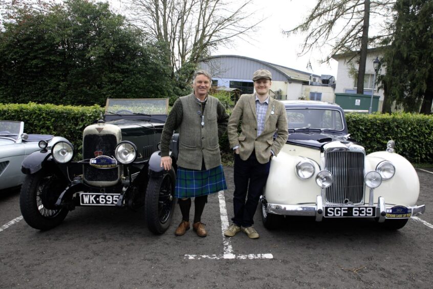 Kilted gather and son in tweed jacket and cap, standing next to two vintage Alvis cars