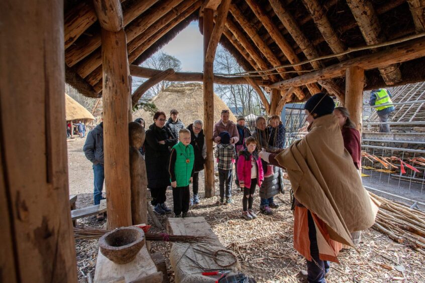 Small crowd of children and adults watches woman make baskets inside timber structure