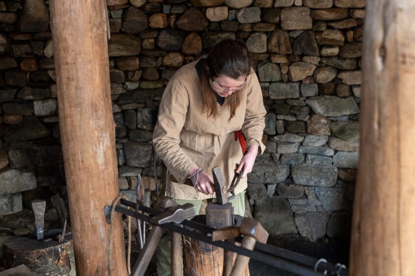 Woman in Iron Age gear bent over an anvil