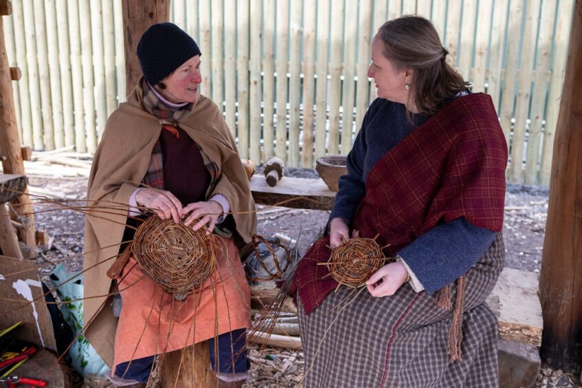 Two women in Iron Age gear making baskets inside wooden structure at Scottish Crannog Centre