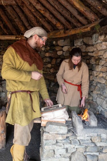 Man and woman at Iron Age forge inside stone building with timber roof