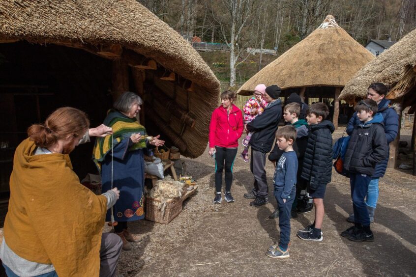 Man and woman in Iron Age gear demonstrating drop spinning to group of young people and adults
