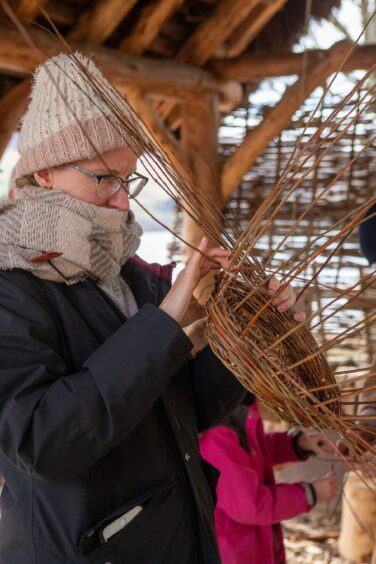 Woman, deep in concentration, making basket inside timber building