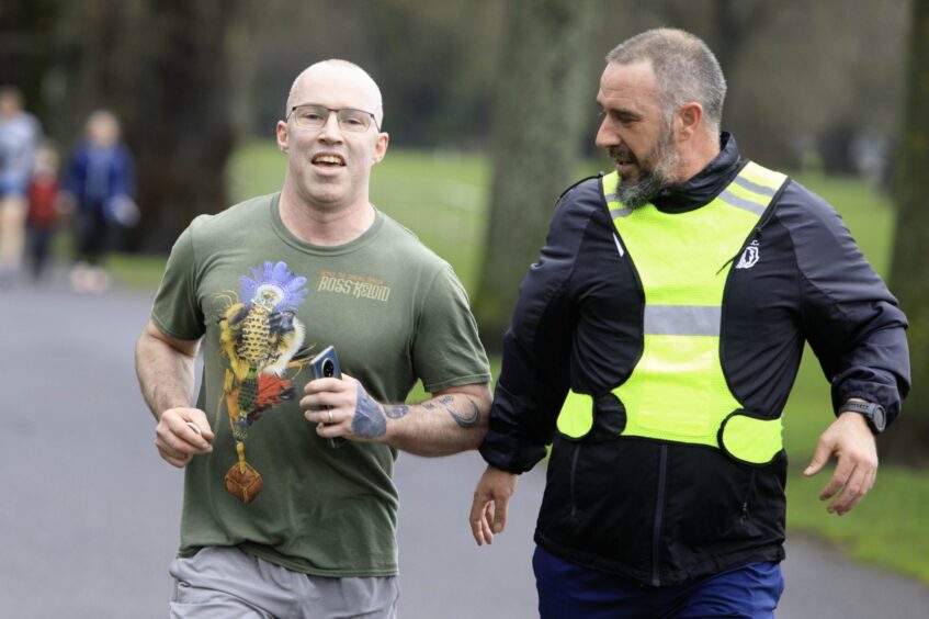 Steven McCready running in Perth parkrun with Charlie King in high vis tunic by his side