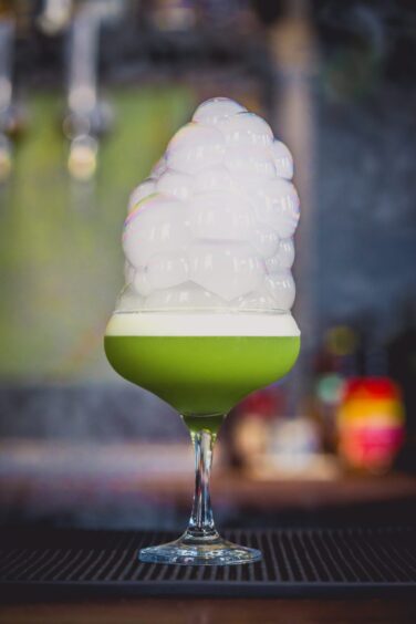 Green cocktail with tall white froth on bar 