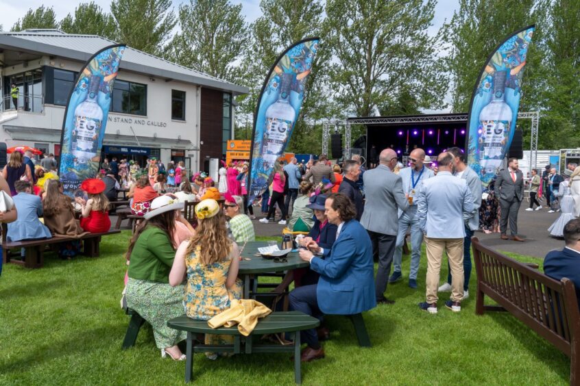 guests sit on picnic tables or stand around the main stage at ladies day at Perth Races