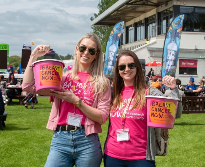 two ladies in pink shirts hold up pink buckets to raise funds for Breast Cancer Now