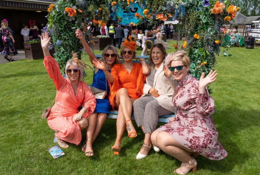 ladies pose for a photo as they sit around a bench decorated with garlands of flowers on a field 