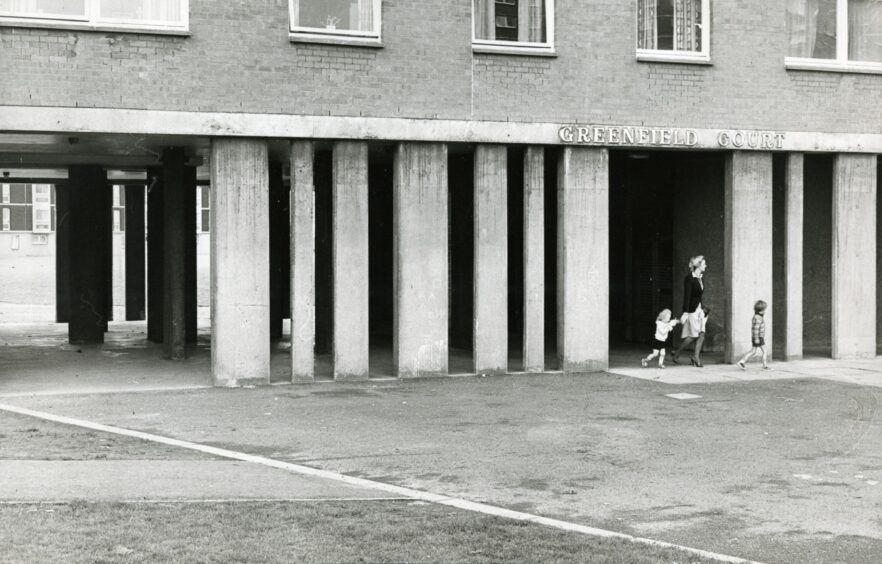 A woman and two children walk beside concrete pillars at the foot of Greenfield Court, Whitfield, Dundee in May 1979