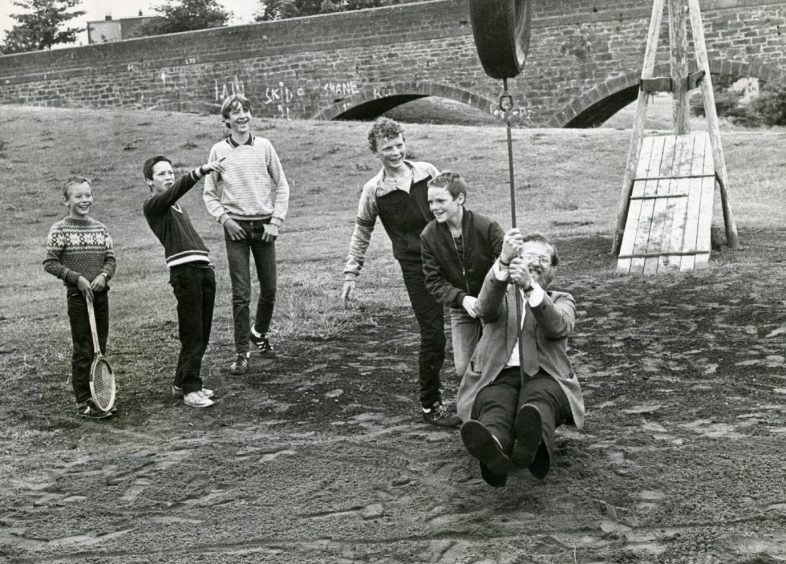 Kids look on and laugh as a man has a go at the aerial runway swing at the adventure park in July 1984. 