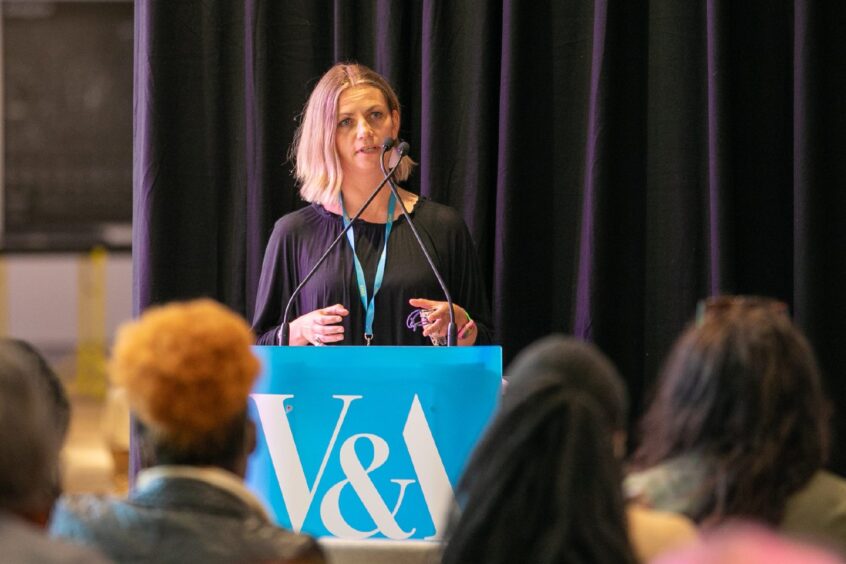 Image shows Leonie Bell, director of the V&A, standing at a podium speaking at an event at the V&A.