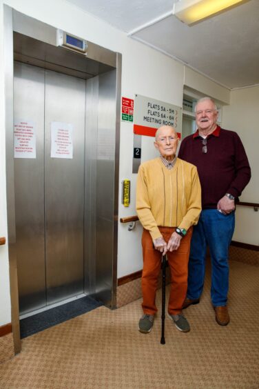 Eddie McHardy and Dewar Court neighbour Jimmy Weir standing next to broken lift with out of order sign on sliding doors