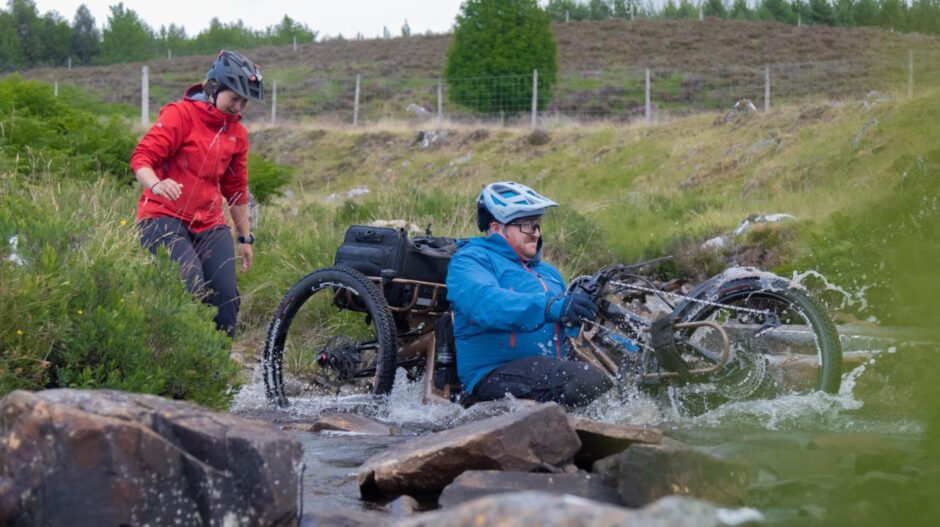 Rosie watches as Neil splashes through a river on his e-assist hand cycle. Image: Stefan Morrocco.