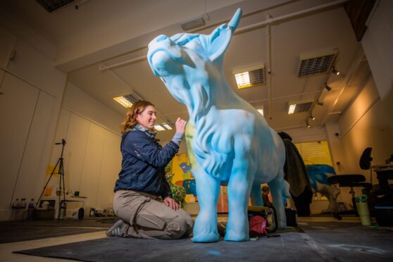 Catherine Briggs kneeling in front of an unpainted Highland cow sculpture.