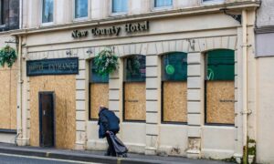 New County hotel exterior with boards over window and building looking neglected